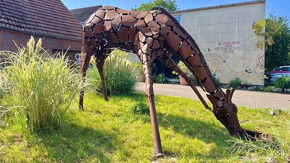 Kunstwerk Giraffe aus Altmetall auf Wiese vor Backsteinhaus
